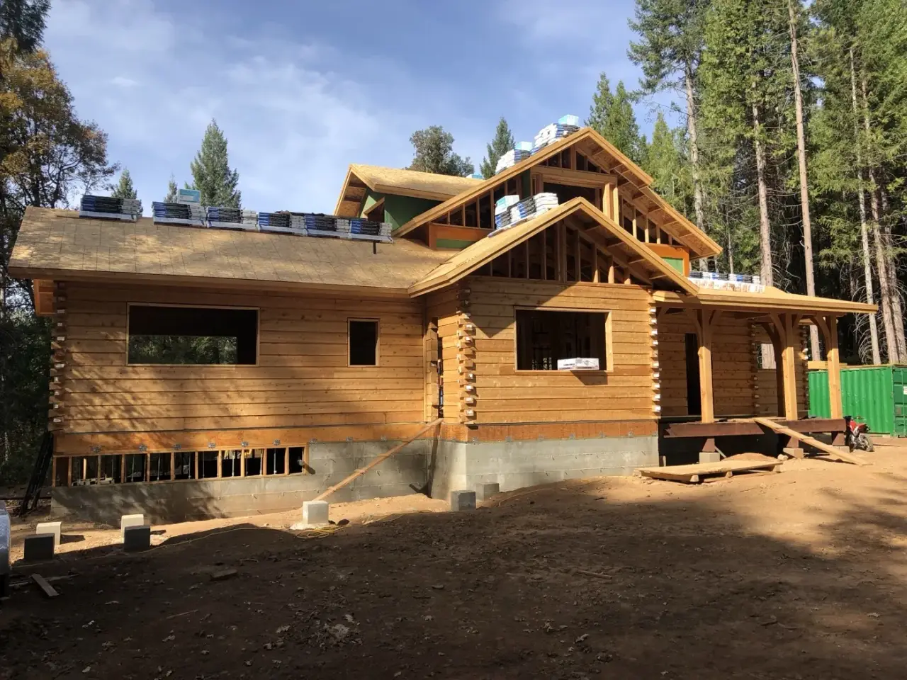 A two story log home nearly dried in, roofing bundles on the papered roof.