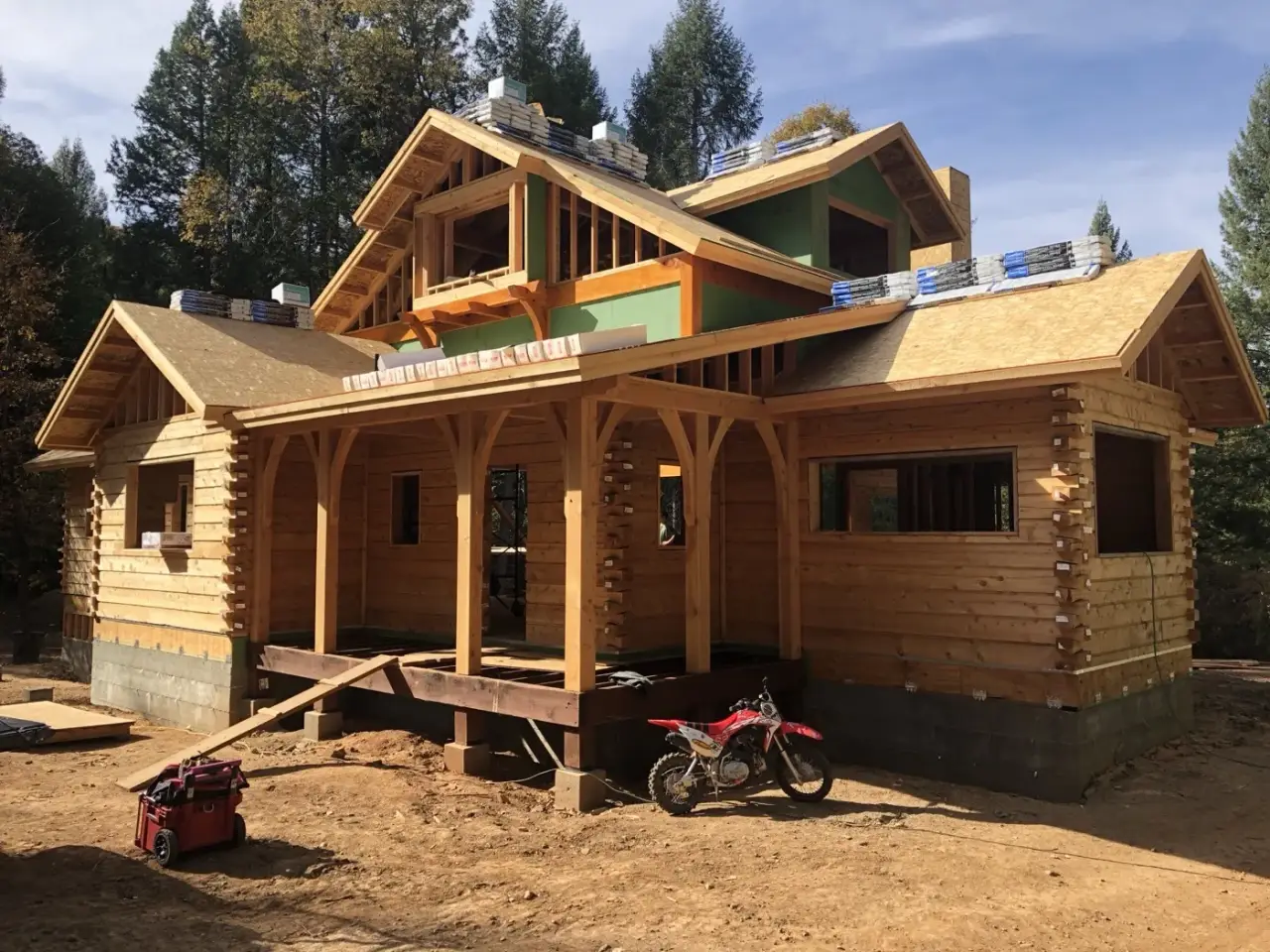 Shingle bundles staged over log walls, arched timber porch framing across the front.
